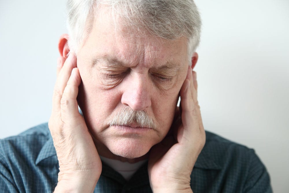 older man holds both hands to his upper jaw near the ears