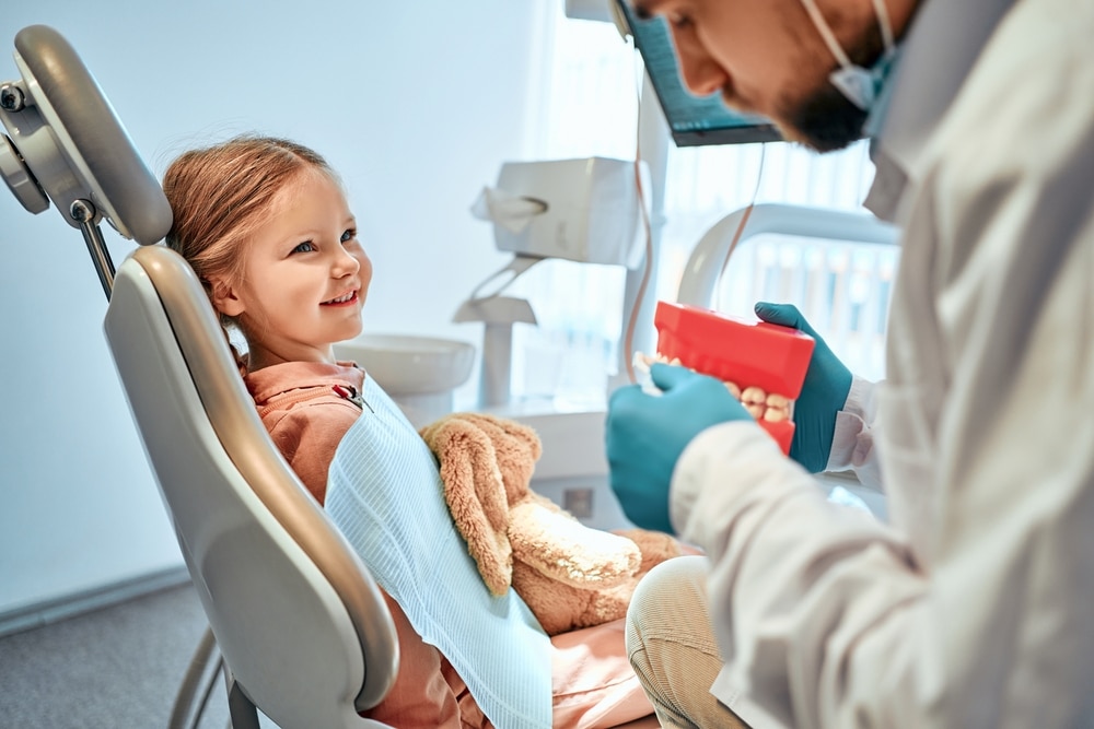 A little girl sits in a dental chair and looks at the doctor